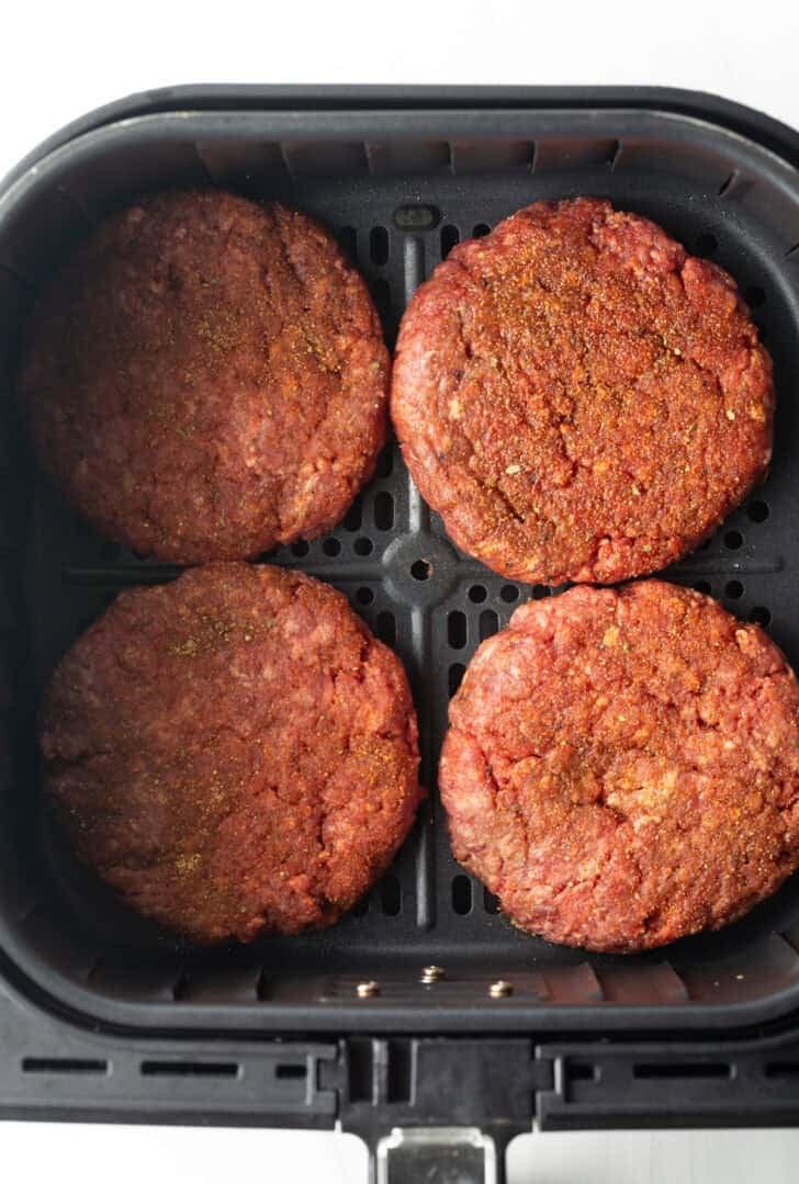 Top down view 4 hamburger patties in an air fryer basket.