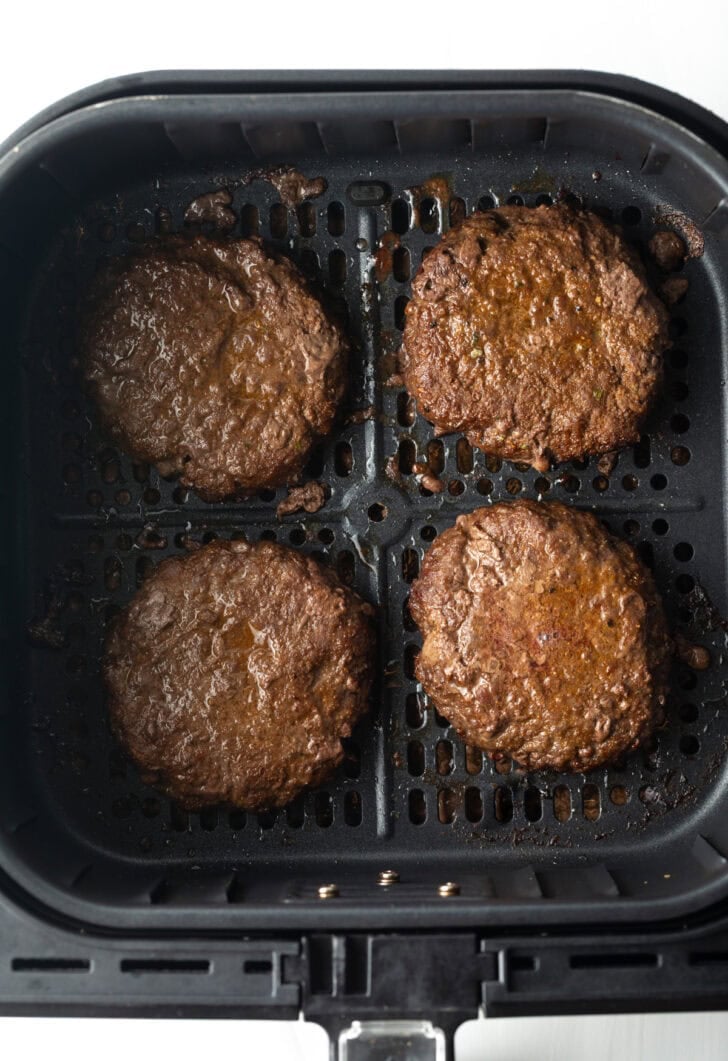 Top down view 4 burgers in an air fryer basket.