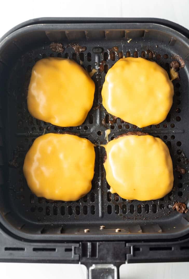 Top down view 4 cheeseburgers in an air fryer basket.