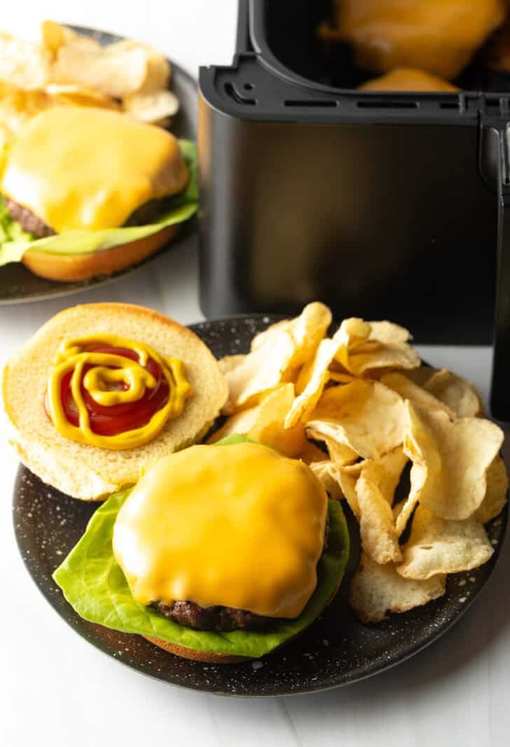 Top down view open faced cheeseburger on a plate with potato chips.