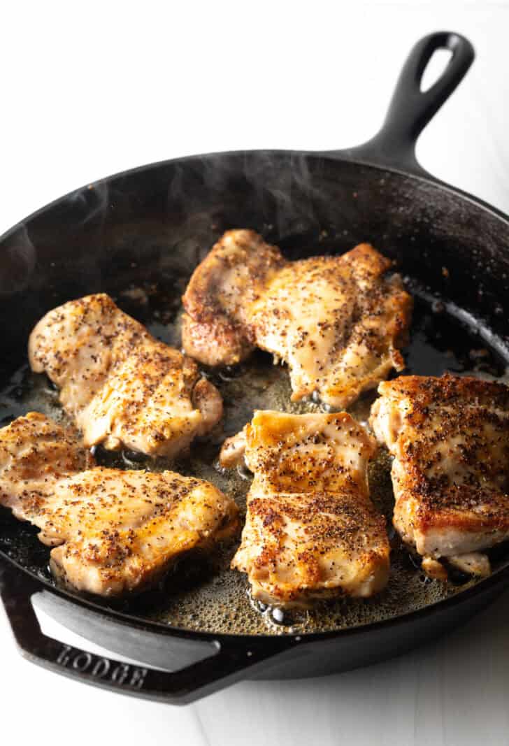 5 cooked chicken thighs in a cast iron skillet.
