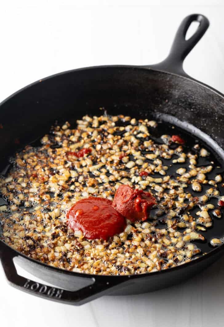 Cooking minced garlic and tomato paste in a cast iron skillet.