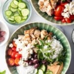 Greek chicken bowl with pieces of chicken, rice, sliced cherry tomatoes, kalamata olives, tzatziki sauce, cucumbers and feta cheese.