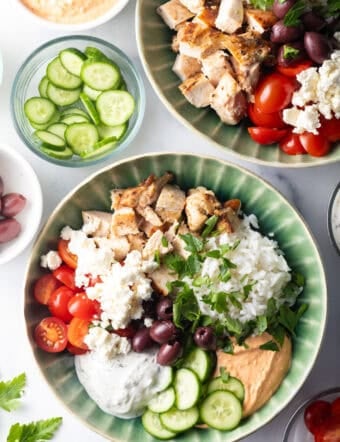 Greek chicken bowl with pieces of chicken, rice, sliced cherry tomatoes, kalamata olives, tzatziki sauce, cucumbers and feta cheese.