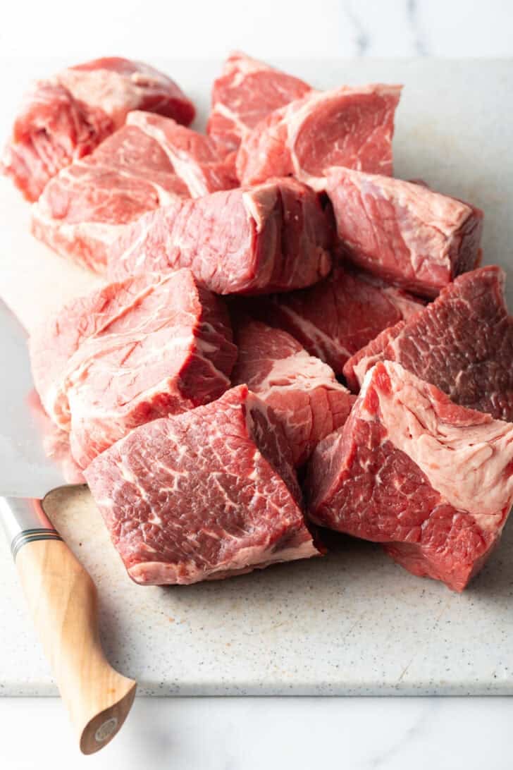 Chunks of raw meat on a cutting board with sharp knife.