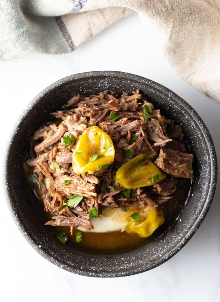 Top down view of a black bowl with a layer of mashed potatoes topped with shredded pot roast and pepperoncinis.