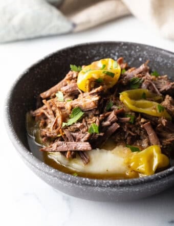 Black bowl with a layer of mashed potatoes topped with shredded pot roast and pepperoncinis.