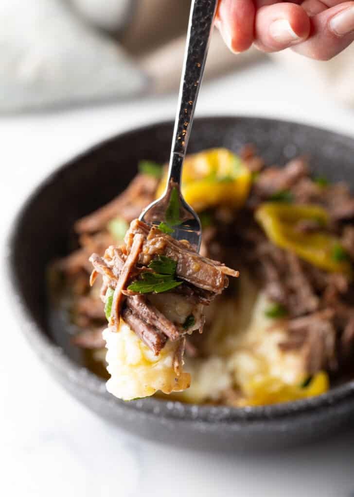 Hand holding a forkful of pot roast to camera.