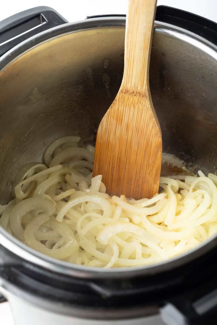 Using a wooden spatula to saute onion slices in an instant pot.