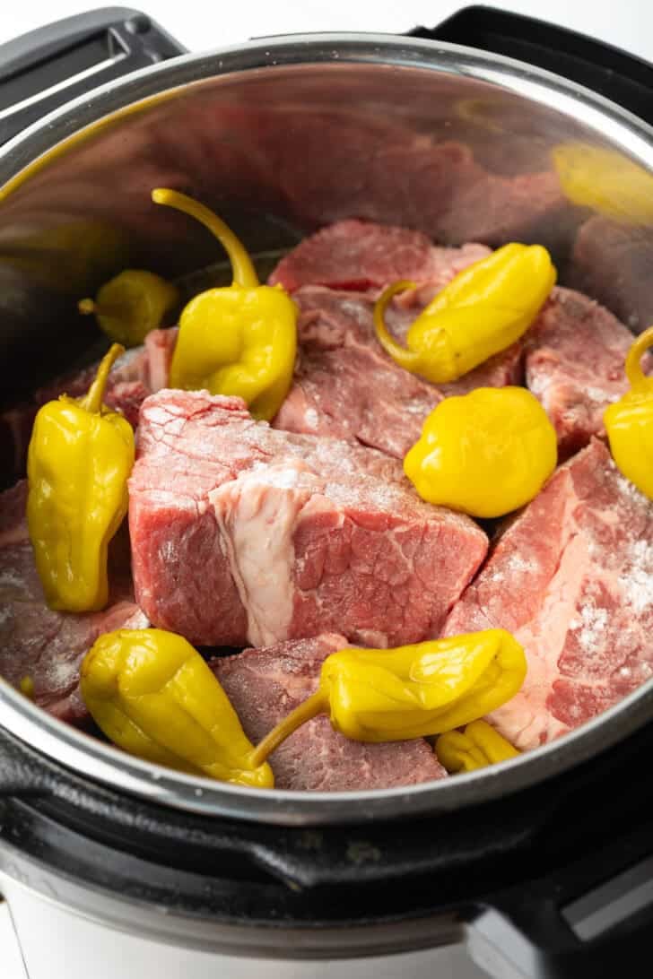 Chunks of raw meat and pepperoncinis in an instant pot.