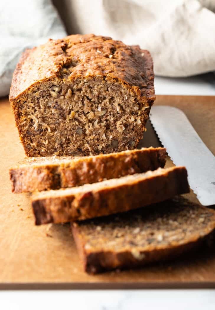 Loaf of moist banana bread on a cutting board, with 3 slices cut and laying in front of the loaf.