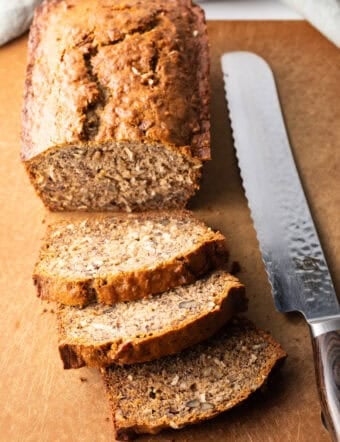 Top down view of a loaf of moist banana bread on a cutting board, with 3 slices cut and laying in front of the loaf.