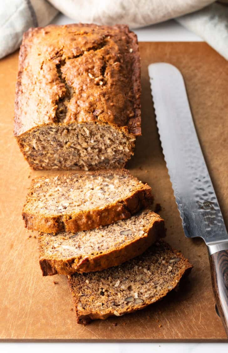 Top down view of a loaf of moist banana bread on a cutting board, with 3 slices cut and laying in front of the loaf.