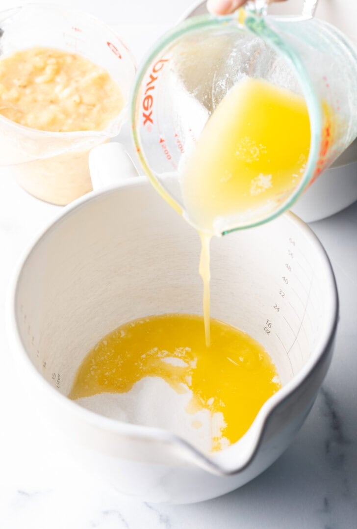 Pouring melted butter from a glass measuring cup into a large white measuring pitcher.