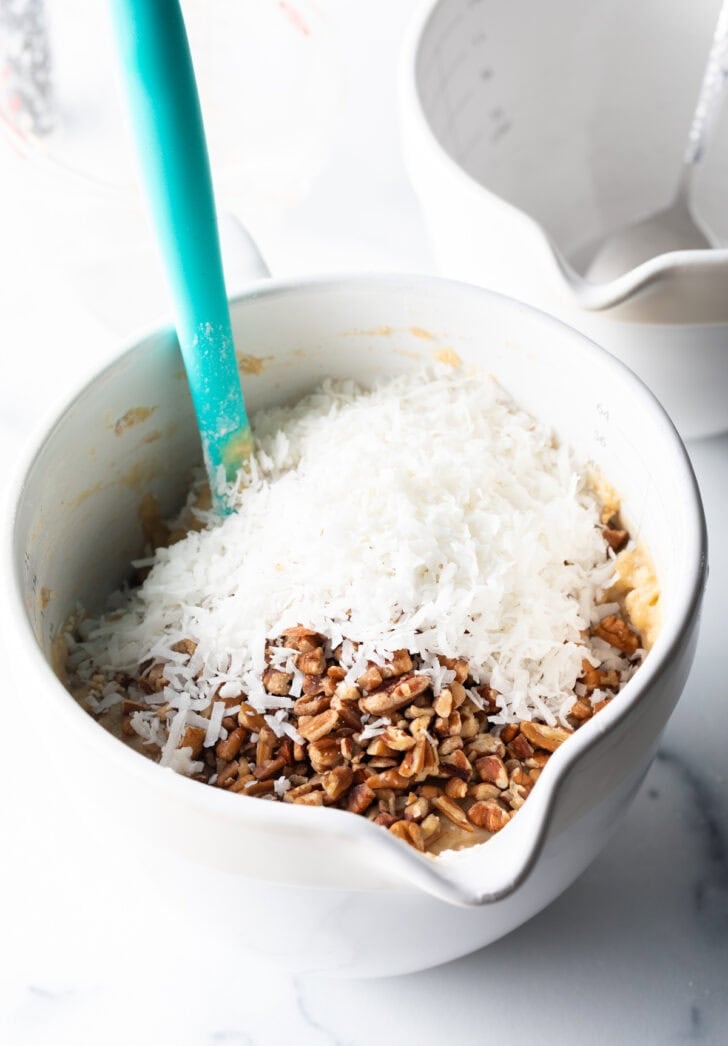 White mixing pitcher with banana bread ingredients and a blue spatula.