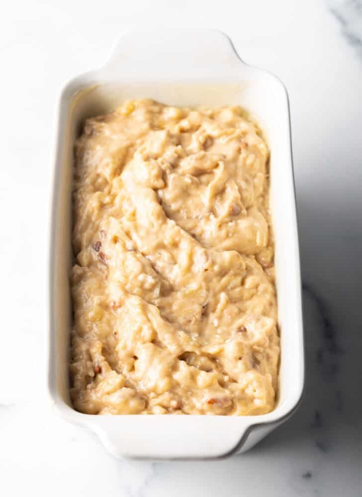 Banana bread batter in a white loaf pan.
