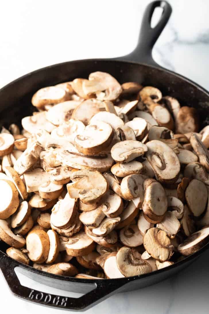 Sliced mushrooms in a cast iron skilet.