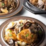 Brown plate with mashed potatoes, topped with two chicken breasts, sliced mushrooms, and gravy.