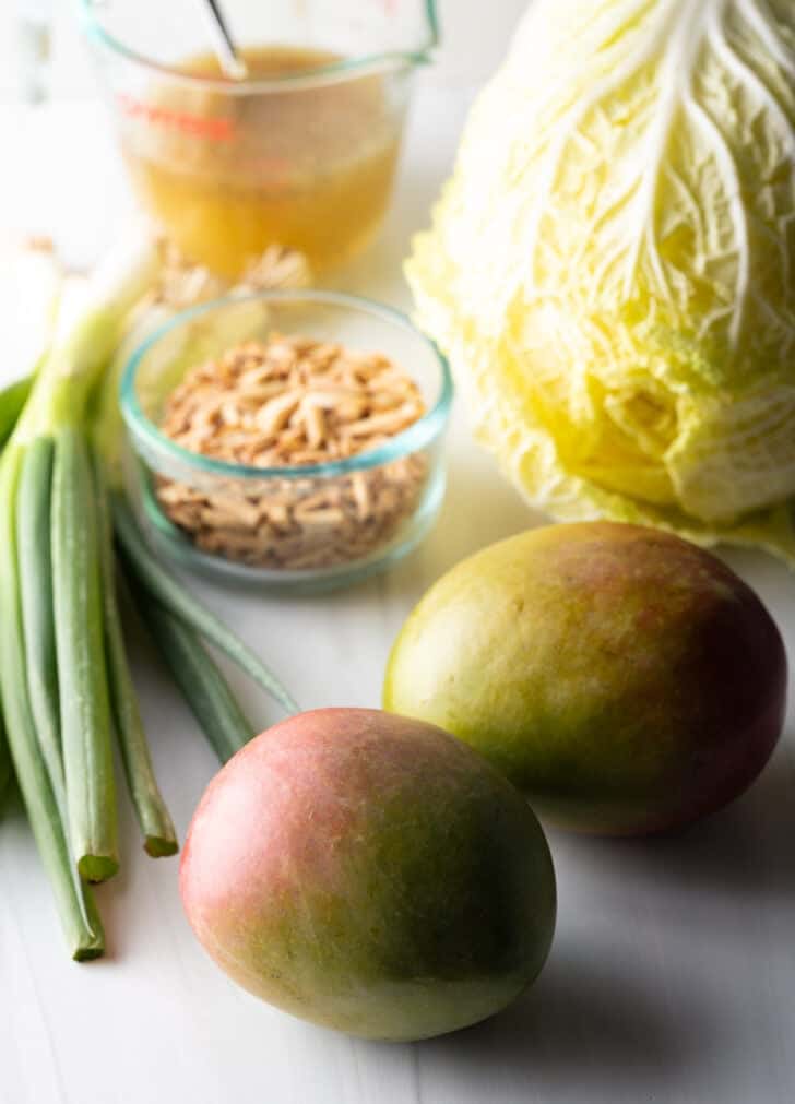 Napa cabbage and mango salad ingredients: 2 whole mangos, bunch of green onions, head of napa cabbage, and glass dish of toasted almonds.