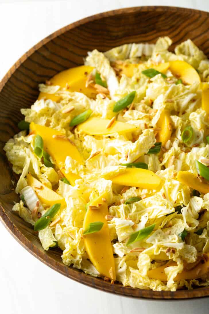 Top down view wood bowl with green napa cabbage, mango slices, and green onions.
