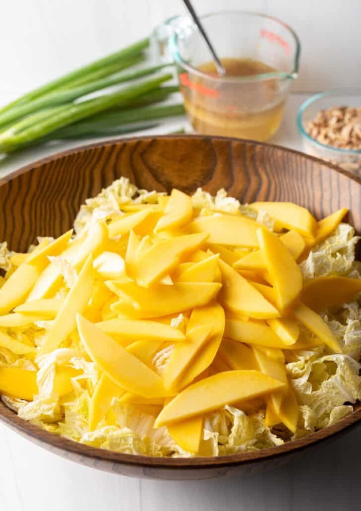 Slices of mango on top of shredded napa cabbage in a wood bowl.