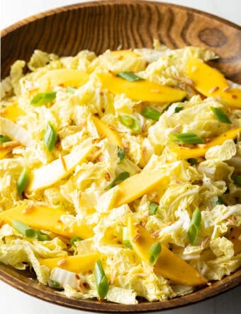Wood bowl with green napa cabbage, mango slices, and green onions.