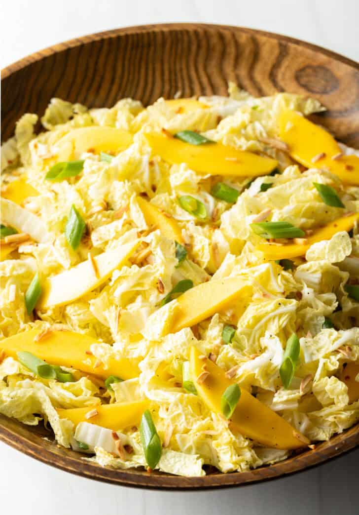 Wood bowl with green napa cabbage, mango slices, and green onions.