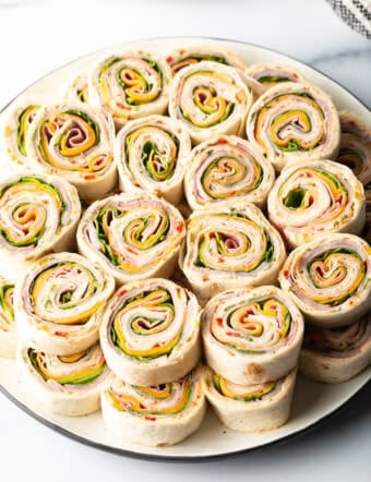 Two layers of a dozen pinwheels stacked on top of each other, on a white round plate.