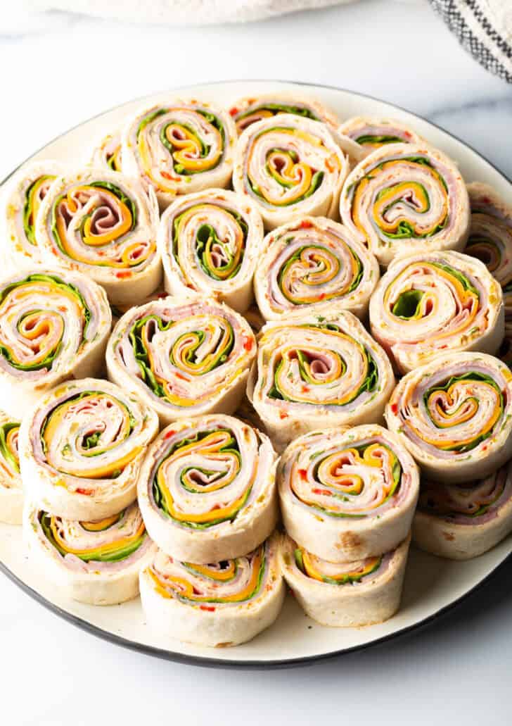 Two layers of a dozen pinwheels stacked on top of each other, on a white round plate.