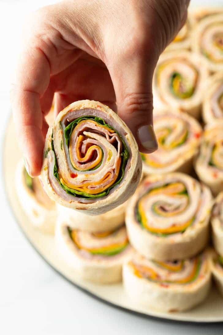 Hand holding a pinwheel wrap with ham, cheese, and spinach.