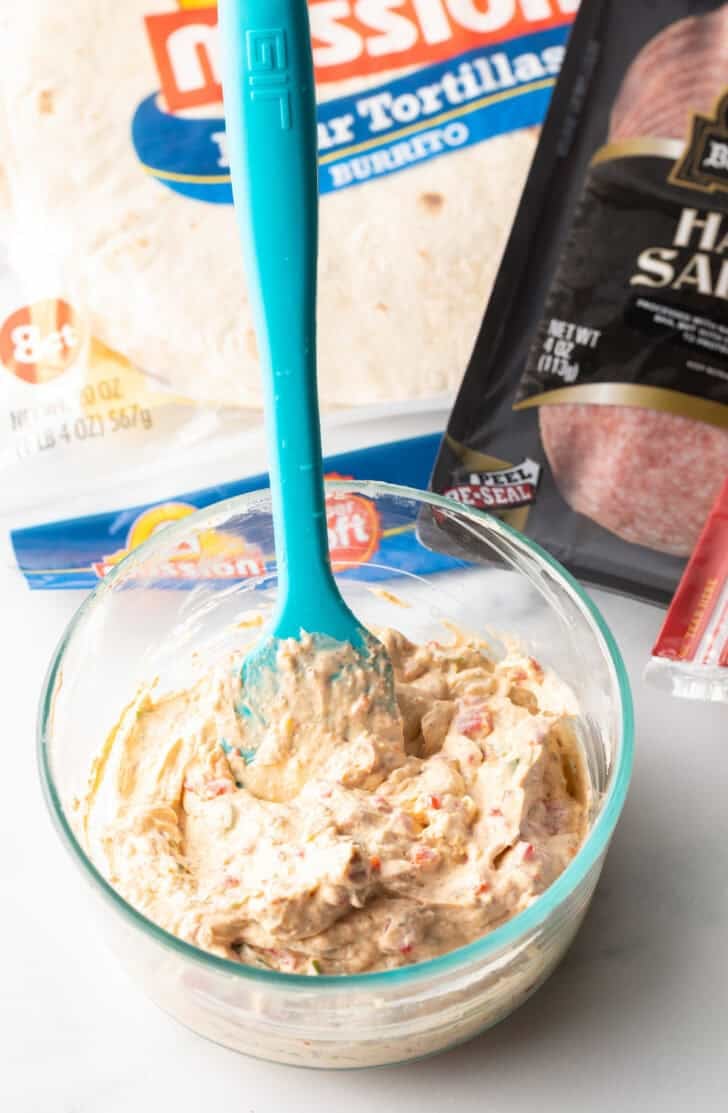Blue spatula stirring together cream cheese mixture in a glass bowl.