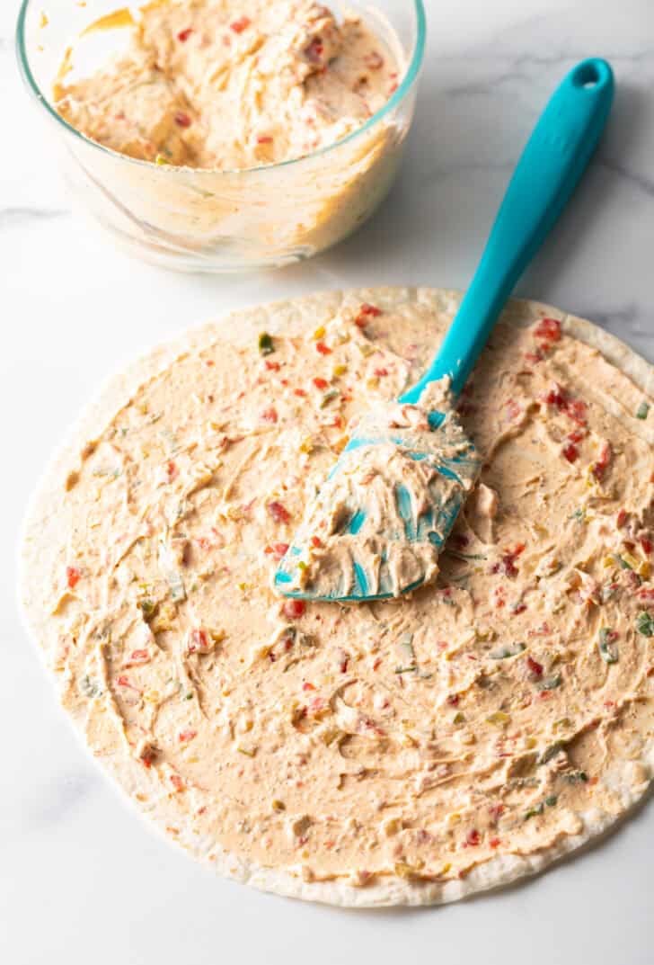Blue spatula spreading cream cheese mixture over a tortilla.