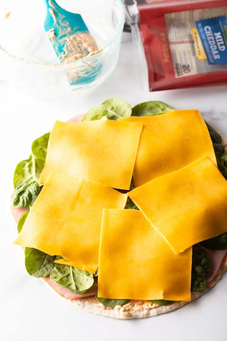 Cheese slices covering spinach leaves on a tortilla.