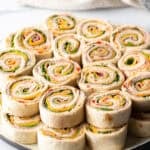 Two layers of a dozen pinwheels stacked on top of each other, on a white round plate.