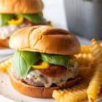 Pizza burger on a white and black speckled plate, with a pile of crinkle cut french fries.