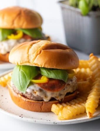 Pizza burger on a white and black speckled plate, with a pile of crinkle cut french fries.