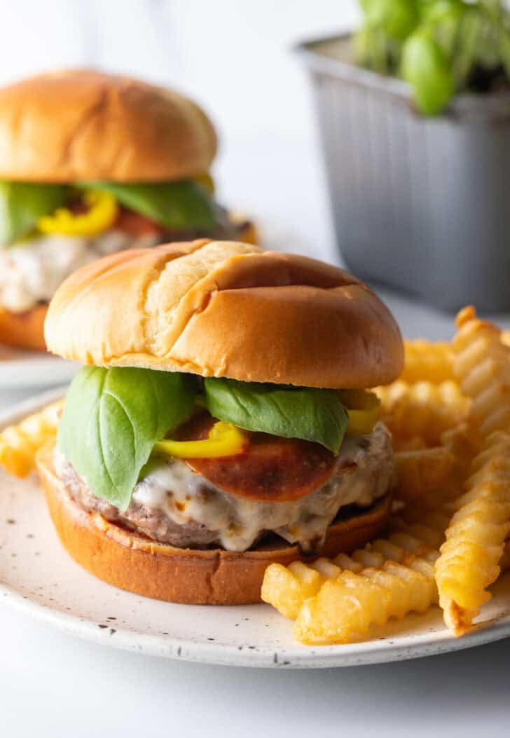 Pizza burger on a white and black speckled plate, with crinkle cut french fries.