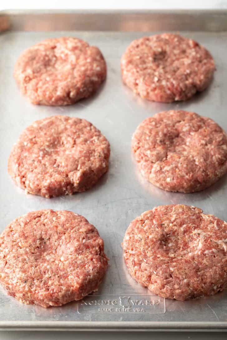 6 raw hamburger pattes on a baking sheet.