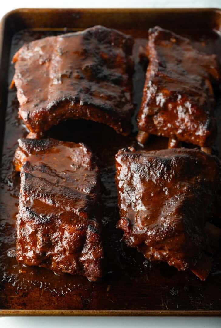 4 sections of cooked baby back ribs on a baking sheet.