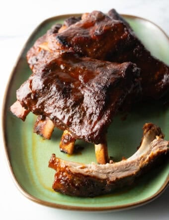 Three 4-piece sections and extra bone of slow cooker ribs on a green plate.
