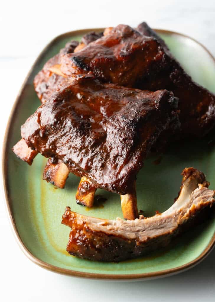 Three 4-piece sections and extra bone of slow cooker ribs on a green plate.