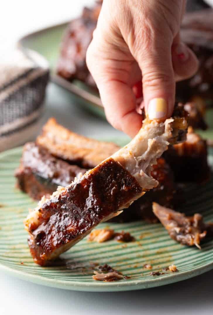 Hand holding a piece of saucy baby back rib to camera.
