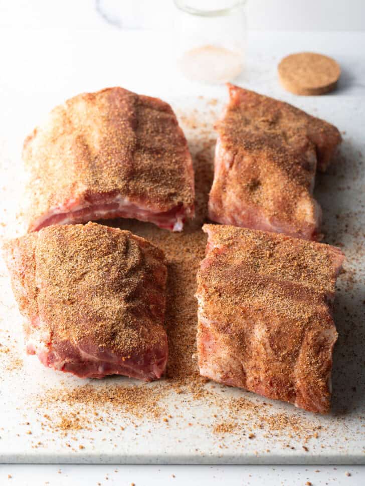 Top down 4 sections of baby back ribs seasoned on a white cutting board.