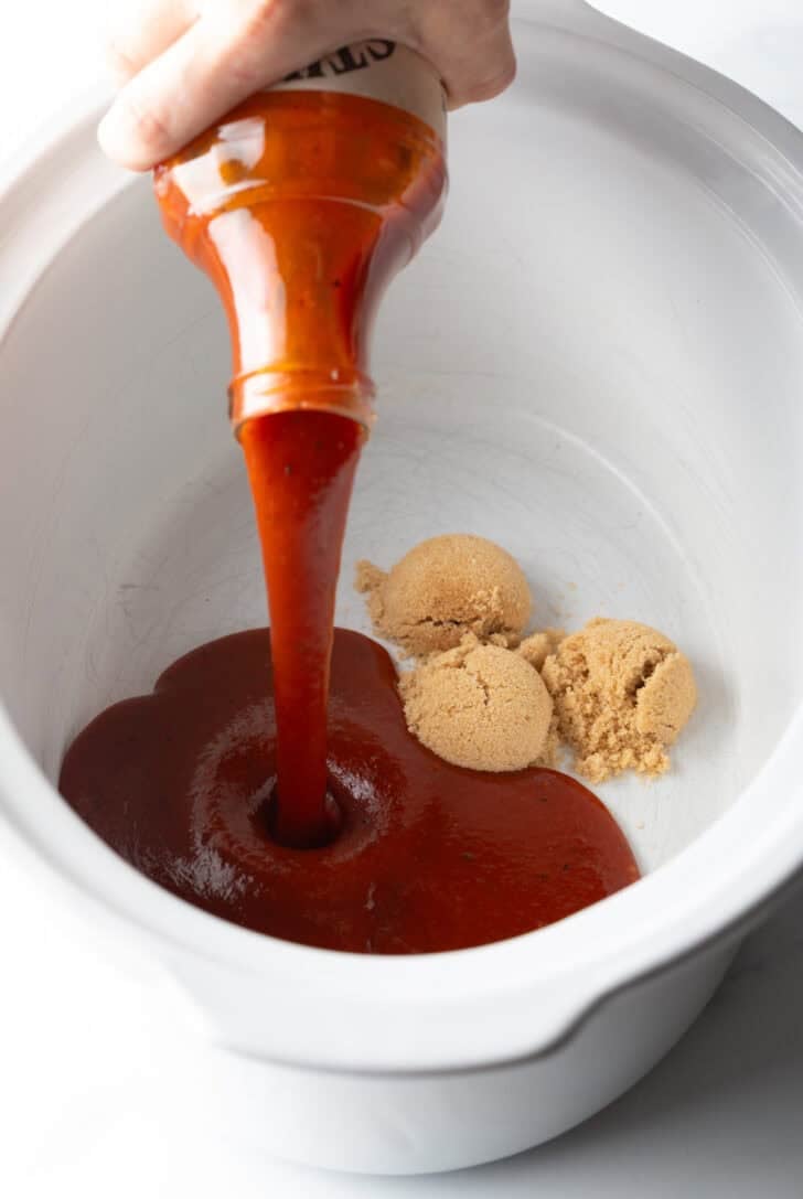 Pouring barbecue sauce into a crock pot with brown sugar.
