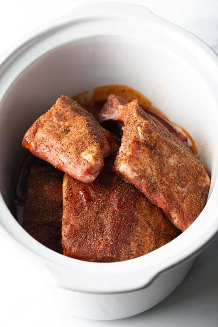 4 raw sections of a rack of ribs in a slow cooker.
