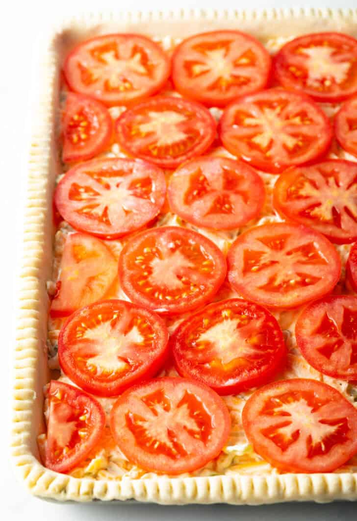 Rows of raw tomato slices on top of an unbaked rectangle of pie dough.