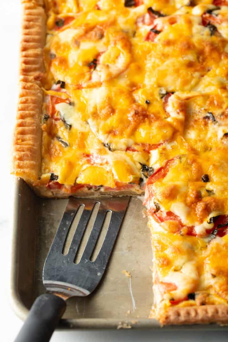 Southern tomato slab pie with large square removed, and a slotted spatula in the pan.