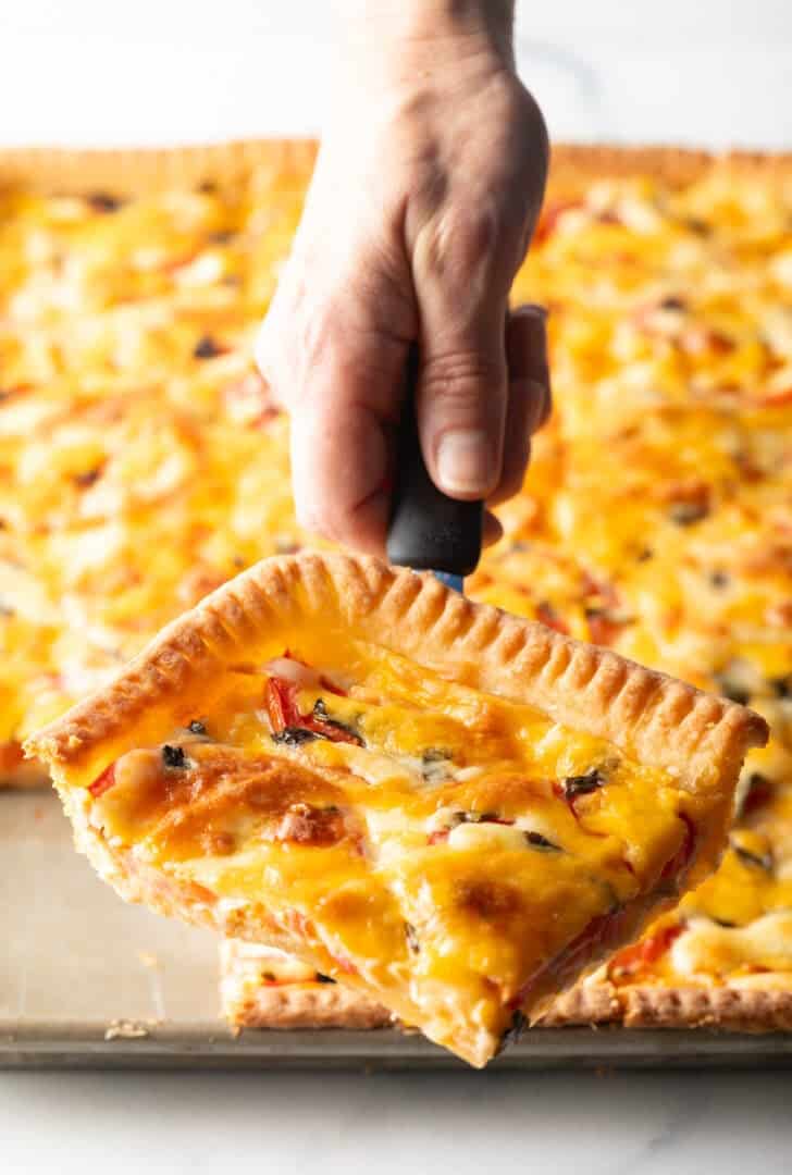 Hand holding a spatula with a large corner square of southern tomato pie.