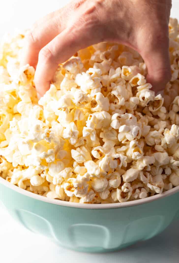 Hand reaching into a blue bowl overflowing with butter popcorn.