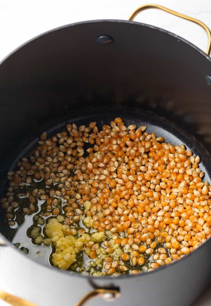 Raw popcorn kernels and ghee in a large black cooking pot.